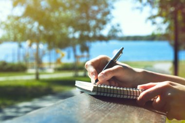 girls hands with pen writing on notebook in park clipart