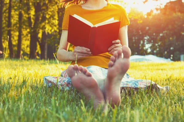 Девушка читает книгу босиком в теплой летней траве — стоковое фото