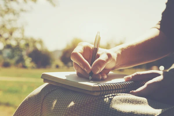 Meisjes handen met pen schrijven op notebook in park — Stockfoto