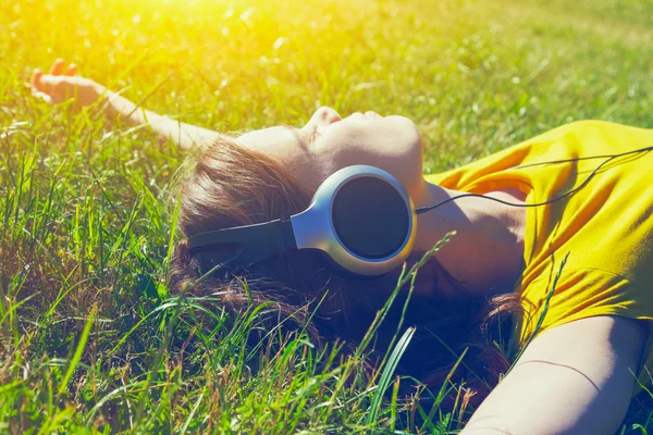 Gadis cantik berbaring di rumput musim panas dengan headphone mendengarkan m — Stok Foto