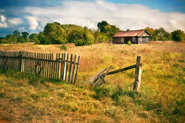 Starý dům s dřevěným plotem na prázdnou louku — Stock fotografie