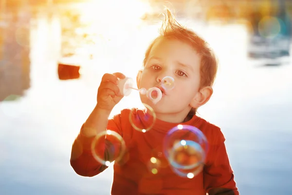 Little boy blowing soap bubbles at a lake — Stock Photo, Image