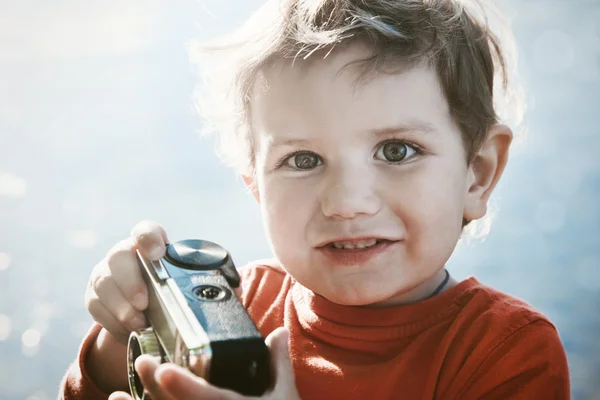 Retrato de um menino bonito sorridente com câmera retro na luz do sol — Fotografia de Stock