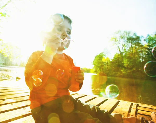 Little boy blowing soap bubbles at a lake — Stock Photo, Image
