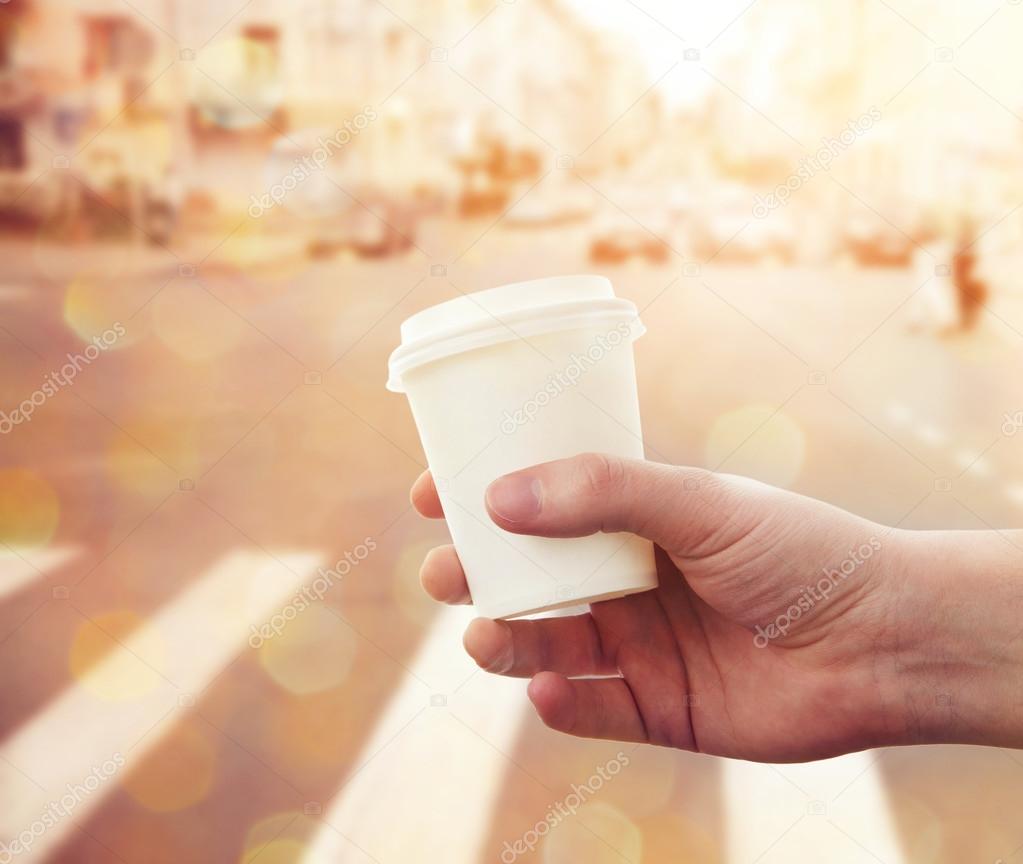 hand holding paper cup with take-out coffee at city street