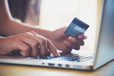 Kredi kartı tutan ve dizüstü bilgisayar kullanan eller. İnternetten alışveriş
