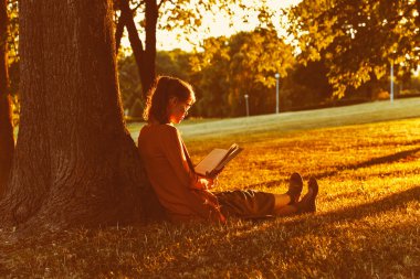 Yazın gün batımında parkta kitap okuyan kız.