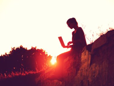 gün batımı veya gündoğumu arka plan üstünde laptop bir kızla silüeti