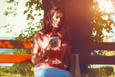 sabah kahve ile bankta oturmuş gülümseyen güzel kız