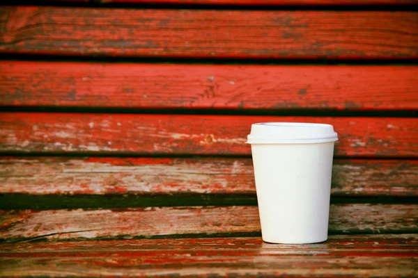 Papieren kopje koffie op houten rode bank als achtergrond — Stockfoto