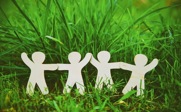 Wooden little men holding hands in summer grass. — Stock Photo, Image