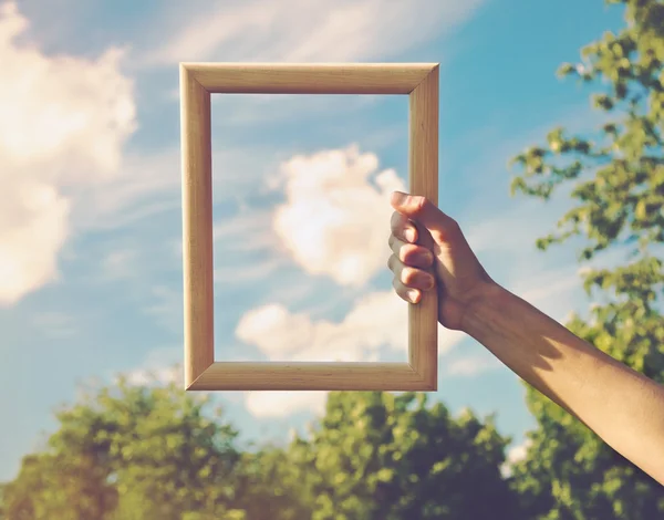 Hand hält einen Holzrahmen auf Wolkenhintergrund. — Stockfoto