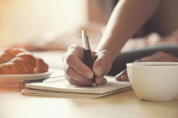 Mani femminili con penna scritta su taccuino con caffè del mattino — Foto Stock