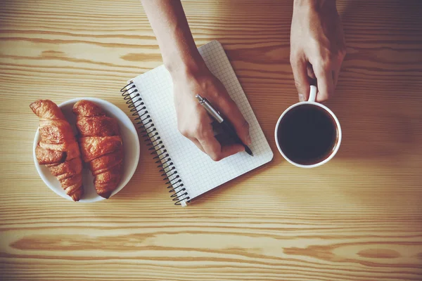 Manos con la escritura de la pluma en el cuaderno con café de la mañana —  Fotos de Stock