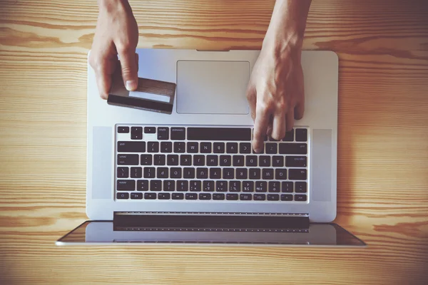 Hands holding credit card and using laptop. View from above — Stock Photo, Image