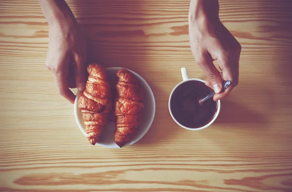 Manos sosteniendo una taza de café y croissants. Vista desde arriba — Foto de Stock