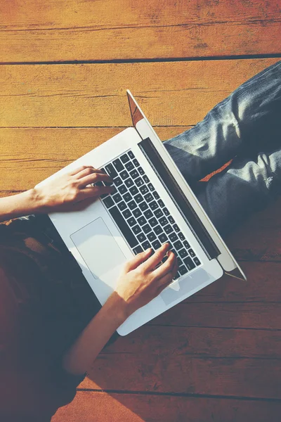 Laptop in Mädchenhänden tippt und sitzt auf einem Holzboden. — Stockfoto