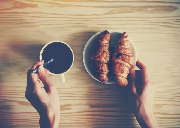 Mãos segurando xícara de café e croissants. Vista de cima — Fotografia de Stock