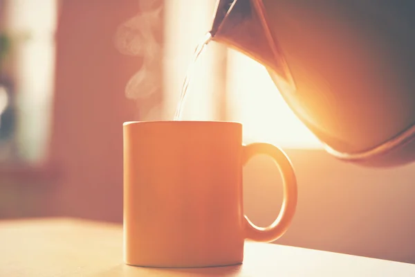 Hervidor de agua vertiendo agua hirviendo en una taza a la luz del sol de la mañana — Foto de Stock