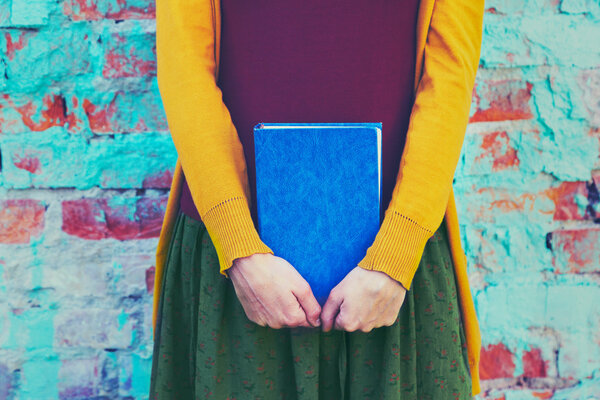 girl holding book in hands on colorful brick wall background
