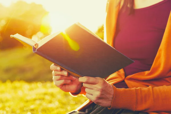 Mãos segurando livro e leitura na luz do pôr do sol verão — Fotografia de Stock