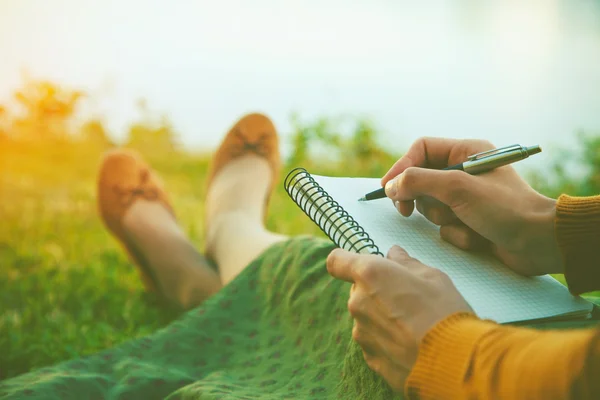 Mani femminili con penna scrittura su taccuino su erba al di fuori — Foto Stock