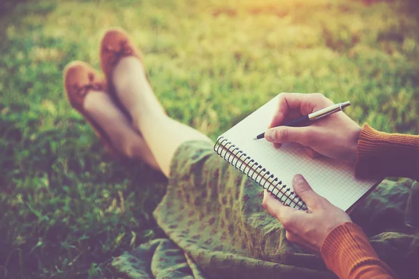 女性的手，用笔在外面的草地上的笔记本上写 — 图库照片