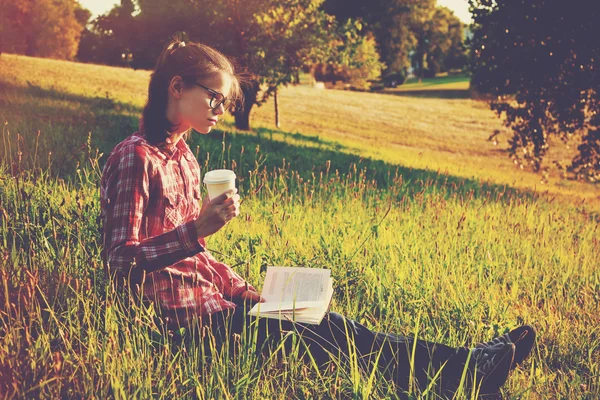 커피 한잔과 책을 여름 잔디에서 즐기는 여자 — 스톡 사진
