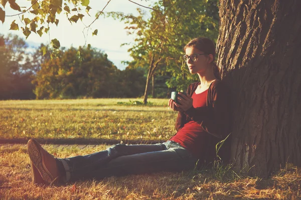 Ragazza sorridente con tazza di tè o caffè godendo vicino all'albero del parco i — Foto Stock