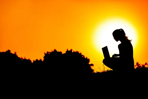 Силуэт девушки с ноутбуком на фоне заката или восхода солнца — стоковое фото