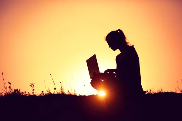 Silhouette d'une fille avec ordinateur portable sur fond de coucher ou de lever du soleil — Photo