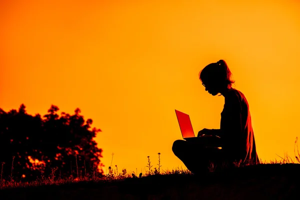 Silhueta de uma menina com laptop no pôr do sol ou nascer do sol fundo — Fotografia de Stock