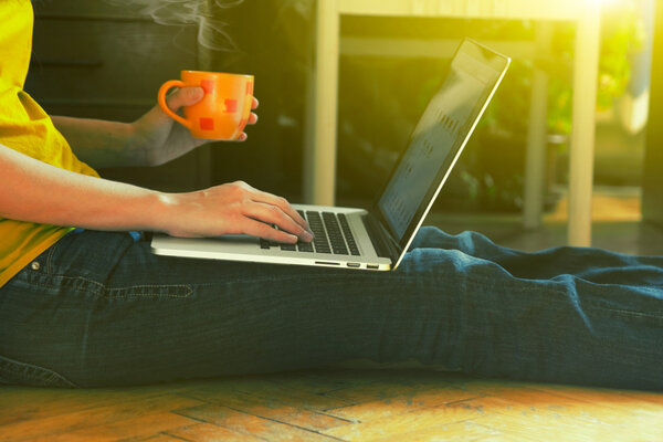 laptop and coffee cup in girls hands sitting on a wooden floor