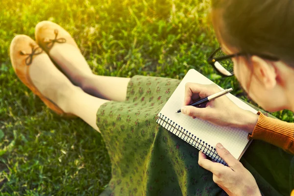 Menina com caneta escrita no notebook na grama fora — Fotografia de Stock