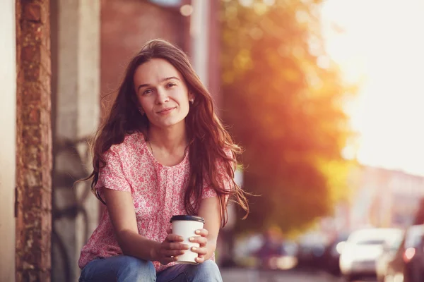 Smiling pretty girl sitting in street with morning coffee — Stock Photo, Image