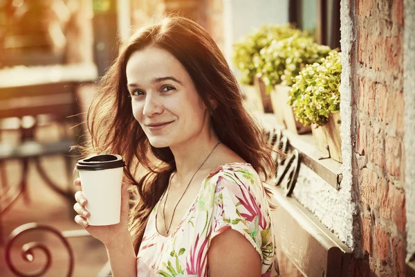Улыбающаяся красивая девушка сидит на скамейке с утренним кофе — стоковое фото
