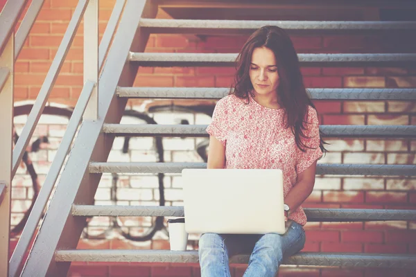 Серьезная девушка работает с ноутбуком, сидя на лестнице лестницы — стоковое фото