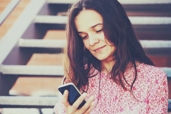 मुस्कुराते सुंदर लड़की स्मार्टफ़ोन पकड़ते हुए और ऐप या पढ़ने का उपयोग करते हुए — स्टॉक फ़ोटो, इमेज