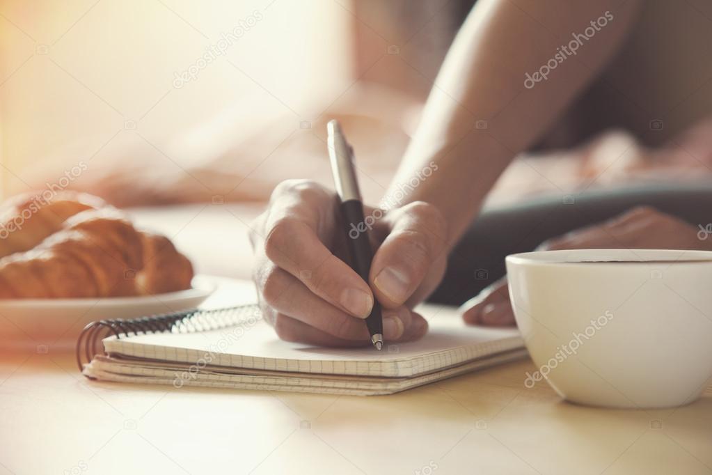 Female hands with pen writing on notebook with morning coffee