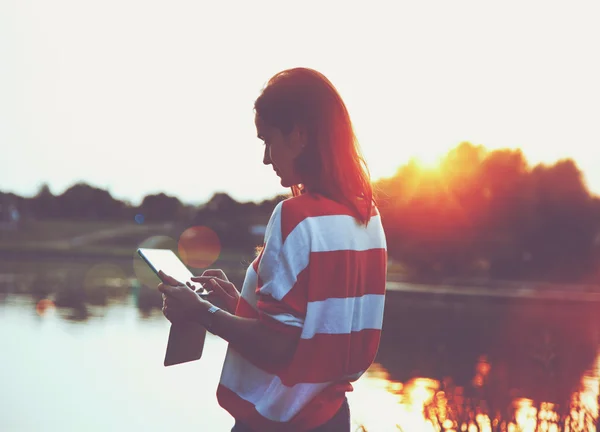 Girl holding digital tablet pc at lake shore in sunrise light — Stock Photo, Image