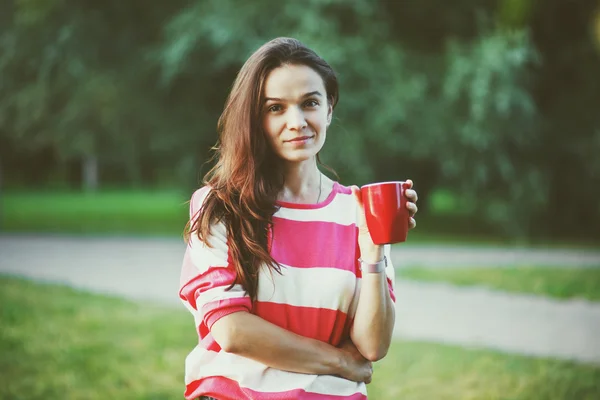 Smiling pretty girl with morning coffee in park — Stock Photo, Image