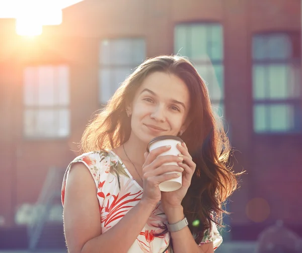 Улыбающаяся красивая девушка, идущая по улице с утренним кофе — стоковое фото
