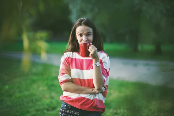 Улыбающаяся красивая девушка с утренним кофе в парке — стоковое фото