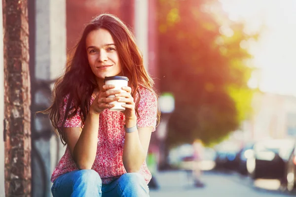 Sonriente chica bonita sentado en la calle con café de la mañana — Foto de Stock