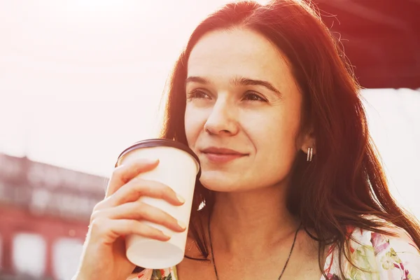 Lachende mooi meisje zit in de straat met koffie in de ochtend — Stockfoto