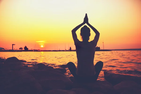 Mulher silhueta praticando ioga posando na praia ao pôr do sol — Fotografia de Stock