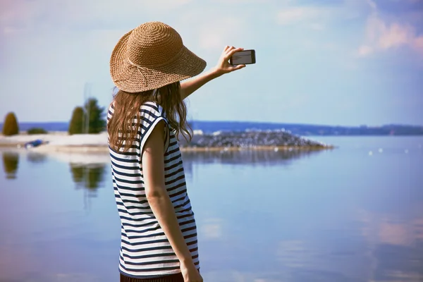 Wanita stylish berdiri sendiri di pantai laut dan mengambil foto dengan — Stok Foto