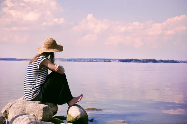 stylish woman alone sitting on stone coast and looking at sea