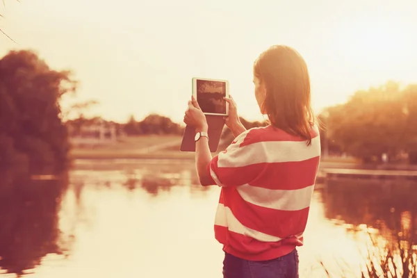 Menina segurando tablet digital pc tirar foto na margem do lago ao sol — Fotografia de Stock