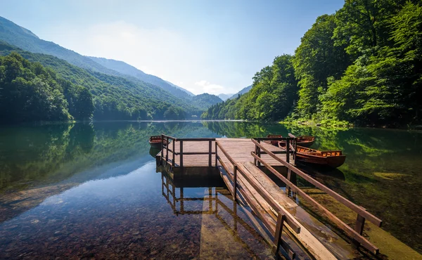 Calma acqua del lago con riflessi di bosco sulle colline e bellissimo vecchio molo di legno — Foto Stock